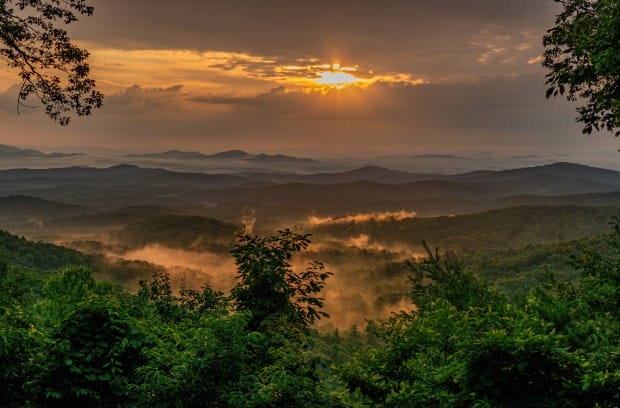 A golden sunrise peeking through the clouds over the Blue Ridge Mountains in Georgia.