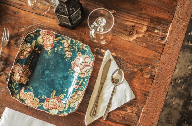 A green antique plate embellished with designs is sitting on a wooden table. Wine glass and silverware are near the plate.