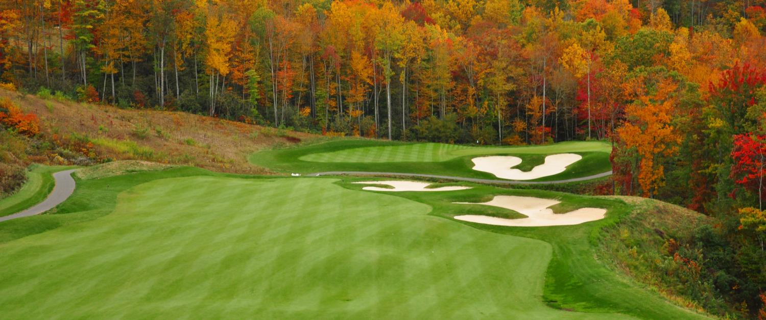 A wide shot shows a well-manicured golf course green in the fall. Gorgeous trees surround the green with vibrant colors.