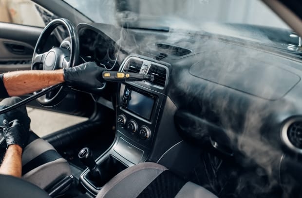 A person wearing black gloves is cleaning a vehicle's interior vents. The vehicle's interior is black.