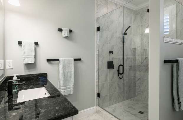 A home bathroom contains a glass walk-in shower, white walls, white vanity, black countertops, and black hardware.