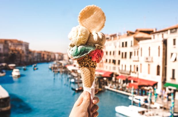 A woman holding a cone of traditional Italian gelato in a cone in front of the historic canals of Venice, Italy.