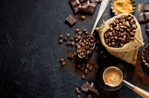 A bag of coffee beans and an espresso capsule with dark roast beans. There's also chocolate on the table near the beans.