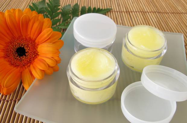 Two small glass containers filled with a yellow substance sit on a glass tray. An orange flower and white lids sit beside them.
