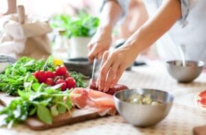 A woman wearing a blue shirt is cutting up a piece of meat in the kitchen. Other cooking ingredients are on the counter.