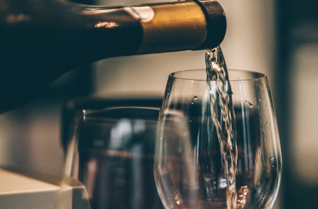 A person is pouring white wine into a long-stemmed wine glass from a dark-colored bottle with a gold label.