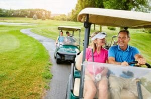 Two couples riding their golf carts on the golf course trail. They're all smiling and enjoying the day.