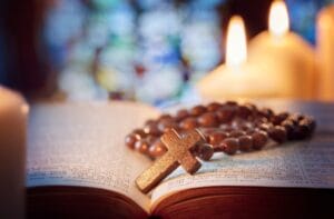 A Catholic rosary sitting on a Bible with the book open. The rosary is wooden with small beads around the cross.
