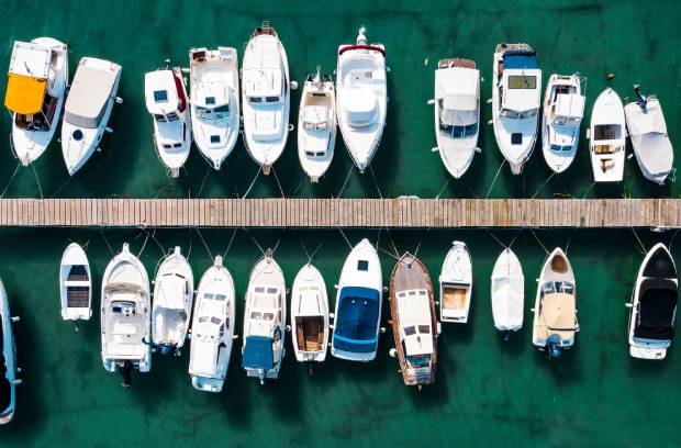 A birds-eye-view of a marina with many different types and sizes of boats docked. A dock in the middle separates the boats.