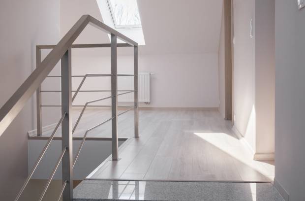 A room in a home contains a gray handrail, light-gray walls, a skylight, and light-gray-colored wooden flooring.