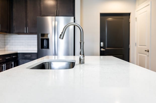 A modern kitchen island with a white quartz countertop, a stainless steel undermount sink, and a silver faucet.