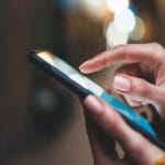 A close-up view shows a person wearing a yellow sweater, holding a cell phone, and scrolling with a finger.