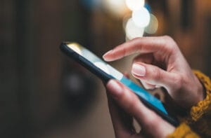 A close-up view shows a person wearing a yellow sweater, holding a cell phone, and scrolling with a finger.