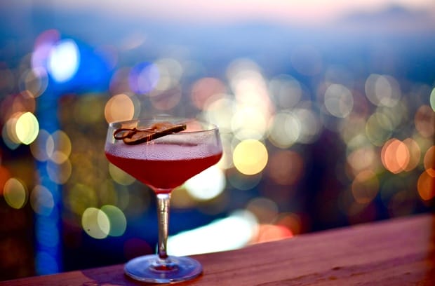 A bar countertop with a martini glass on it. The martini is dark pink in color with a garnish on the rim of the glass.