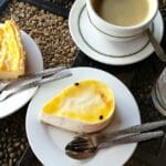 A close-up shot of a table with two plates of dessert set out next to a cup and saucer of coffee and a glass of water.