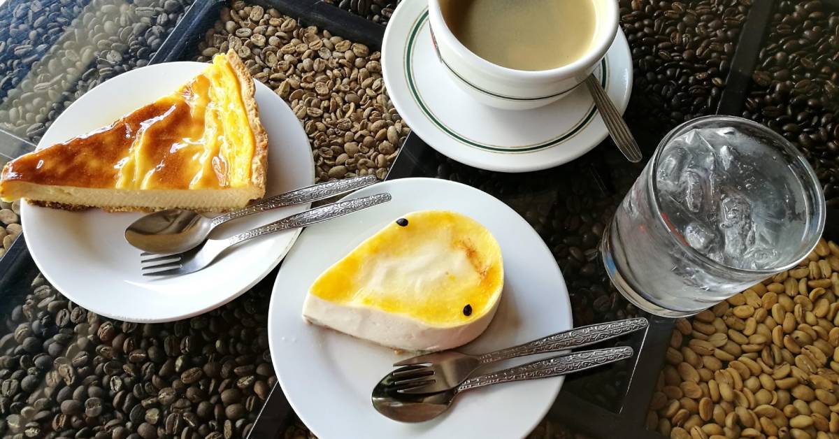 A close-up shot of a table with two plates of dessert set out next to a cup and saucer of coffee and a glass of water.