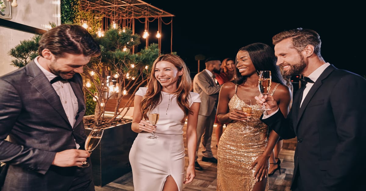 A group of people in beautiful formalwear talking and smiling while enjoying time at a formal event.