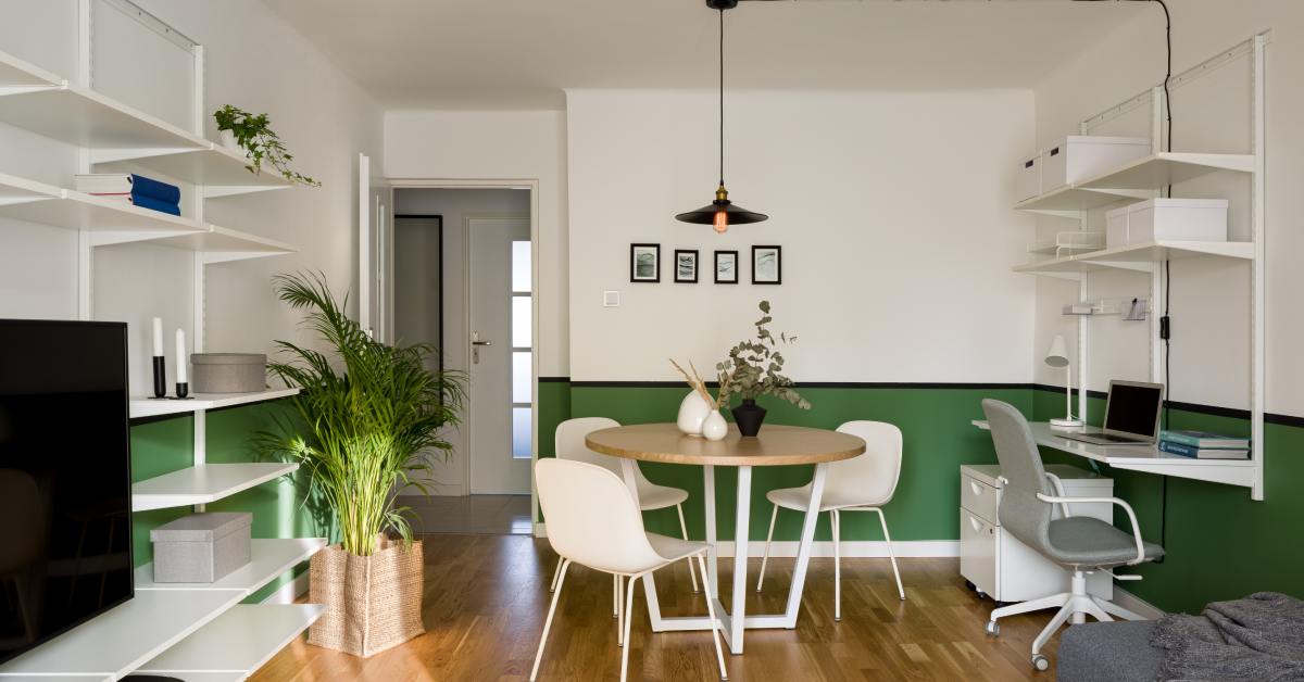 Small apartment with wooden floors, white furniture and cabinets, some plants, a TV, and white green walls.