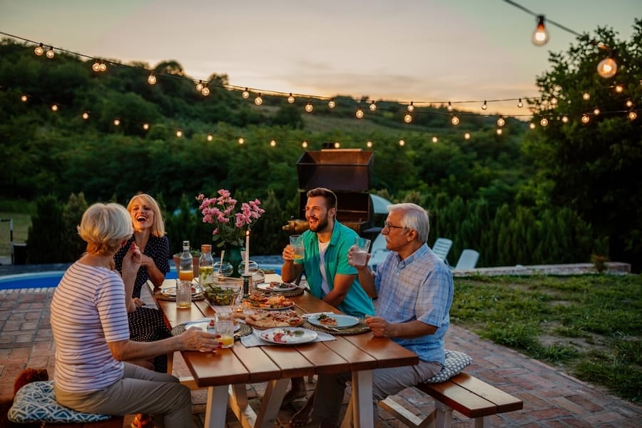 Happy family eating together outdoors. Smiling generation family sitting at dining table during dinner. Happy cheerful family enjoying meal together in garden.