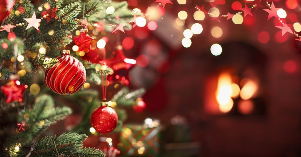 A close-up of a Christmas tree with warm white lights, red decorative ornaments with gold accents, and stars wrapped around.