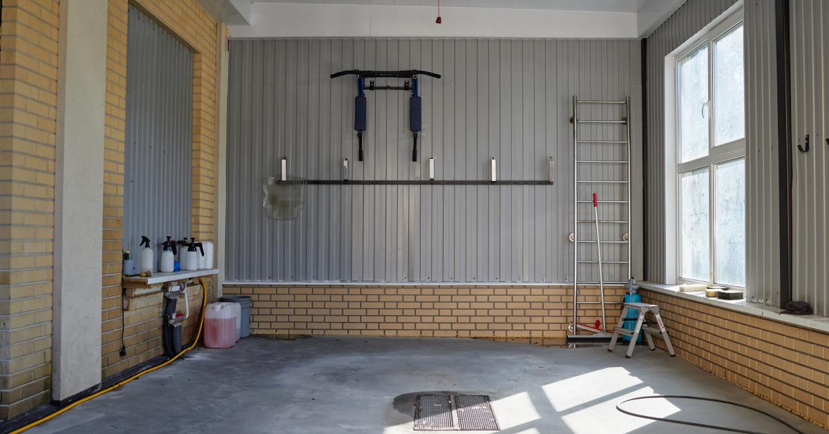 A clean garage contains a gray slatwall, a metal ladder, a yellow cord, a black cord, and a metal step stool.