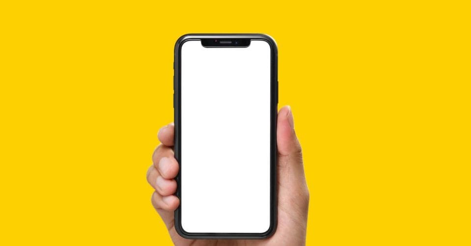 A hand holds up an iPhone that features a blank, white screen. The phone is held against a yellow background.