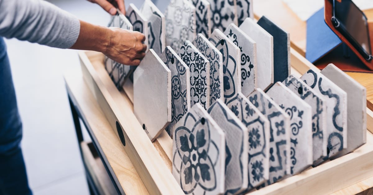 There are two people looking at a selection of tiles. The tiles are all on a stand and they each have intricate designs.