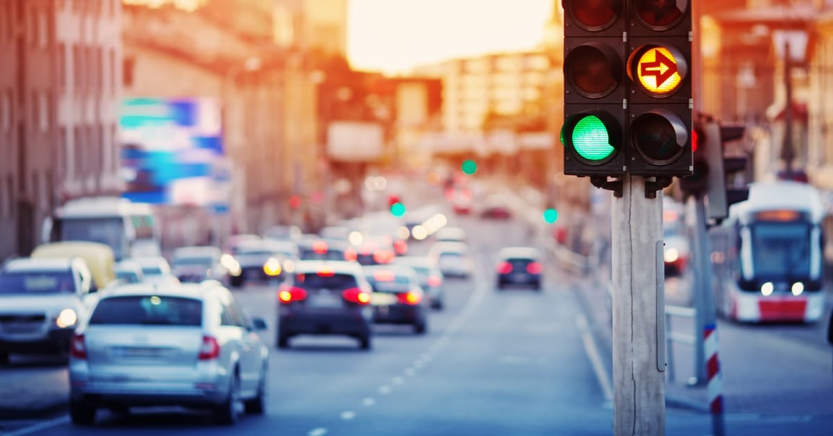 A streetlight with a green light and a yellow turn signal light. Cars are driving into the background behind it.